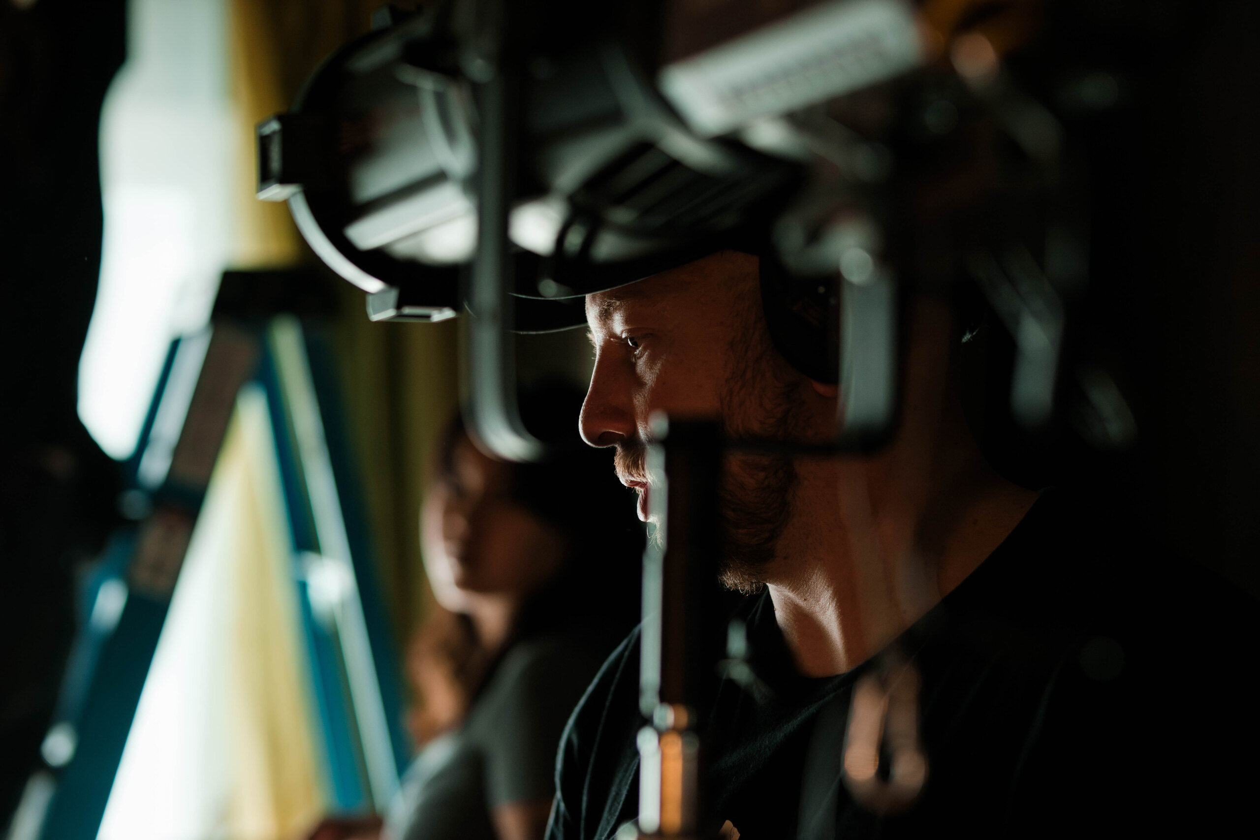 A crew member watches from beside the camera, headphones on.