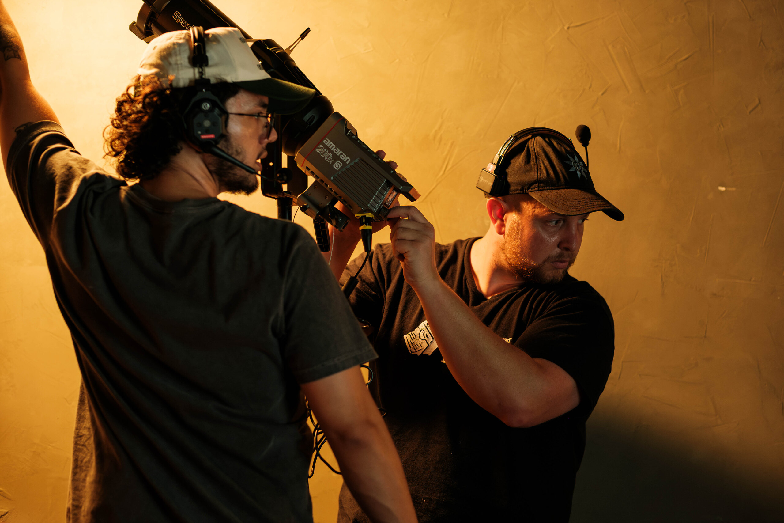 Two crew members handle a lamp against the warm wall.